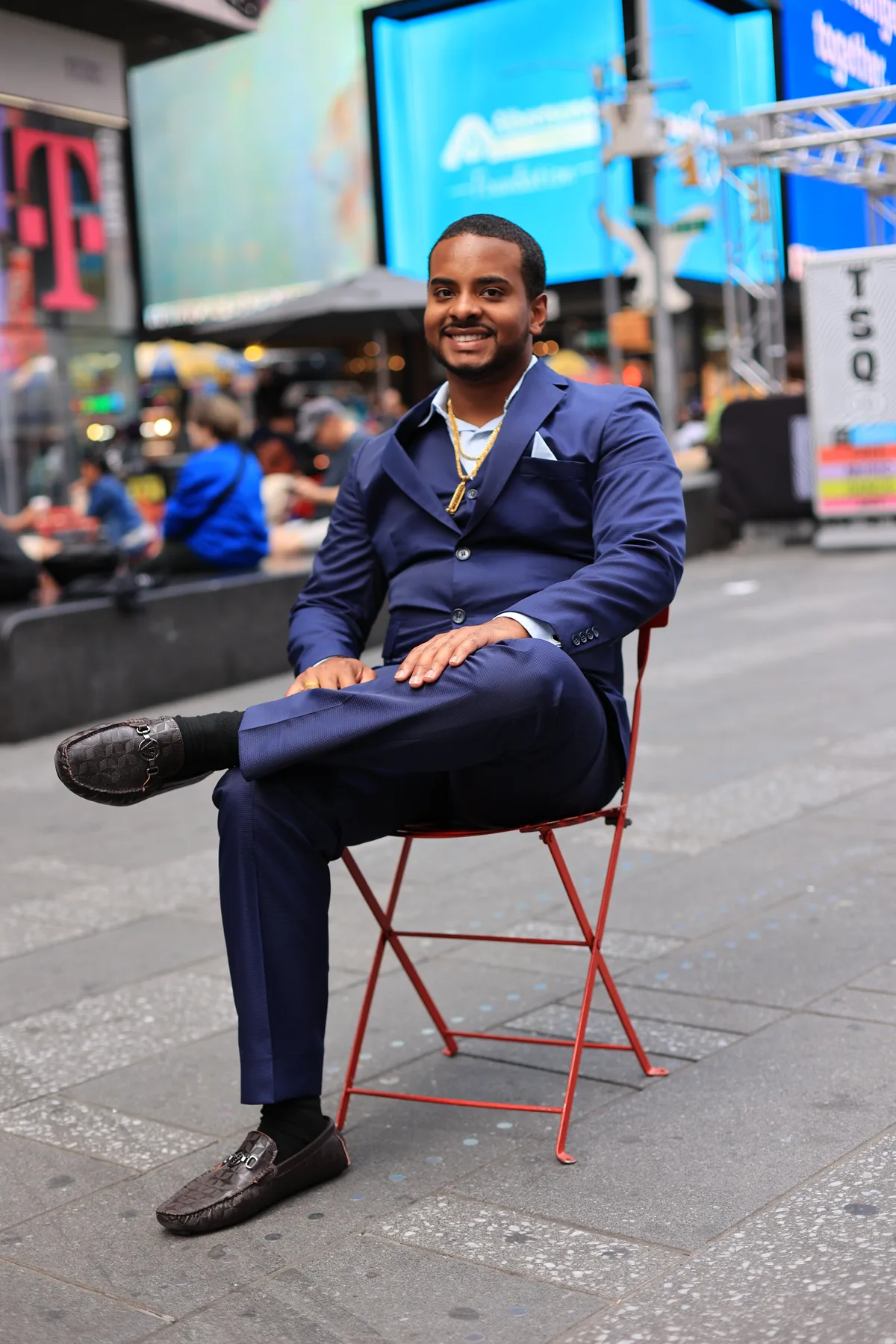 Charles Velazquez seated in Times Square wearing a navy suit